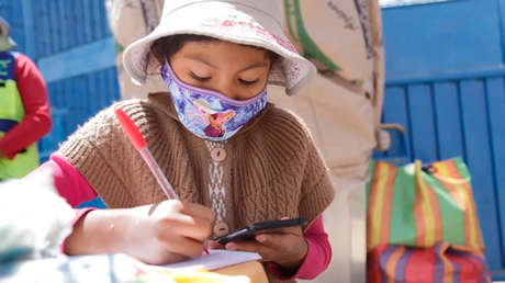 Niña estudia desde un celular mientras ayuda a su tía en puesto de venta de refrescos
